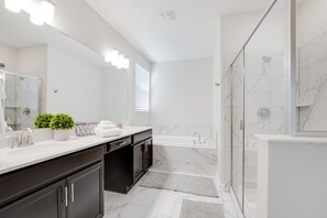 A modern bathroom with a large mirror, white marble tiles, a glass-enclosed shower, and a dark wooden vanity.