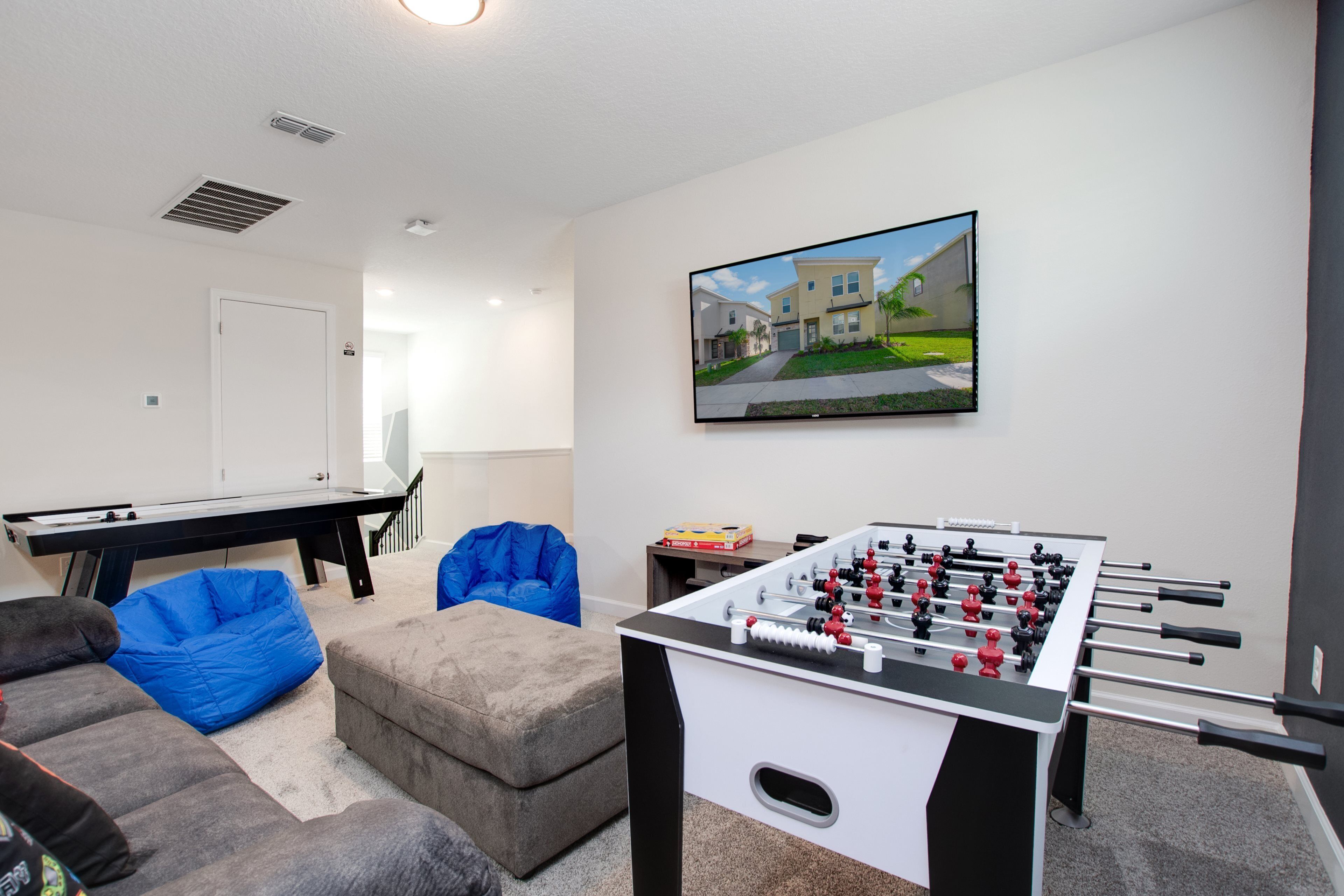 A living room with a foosball table, a pool table, blue bean bags, and a television mounted on the wall.