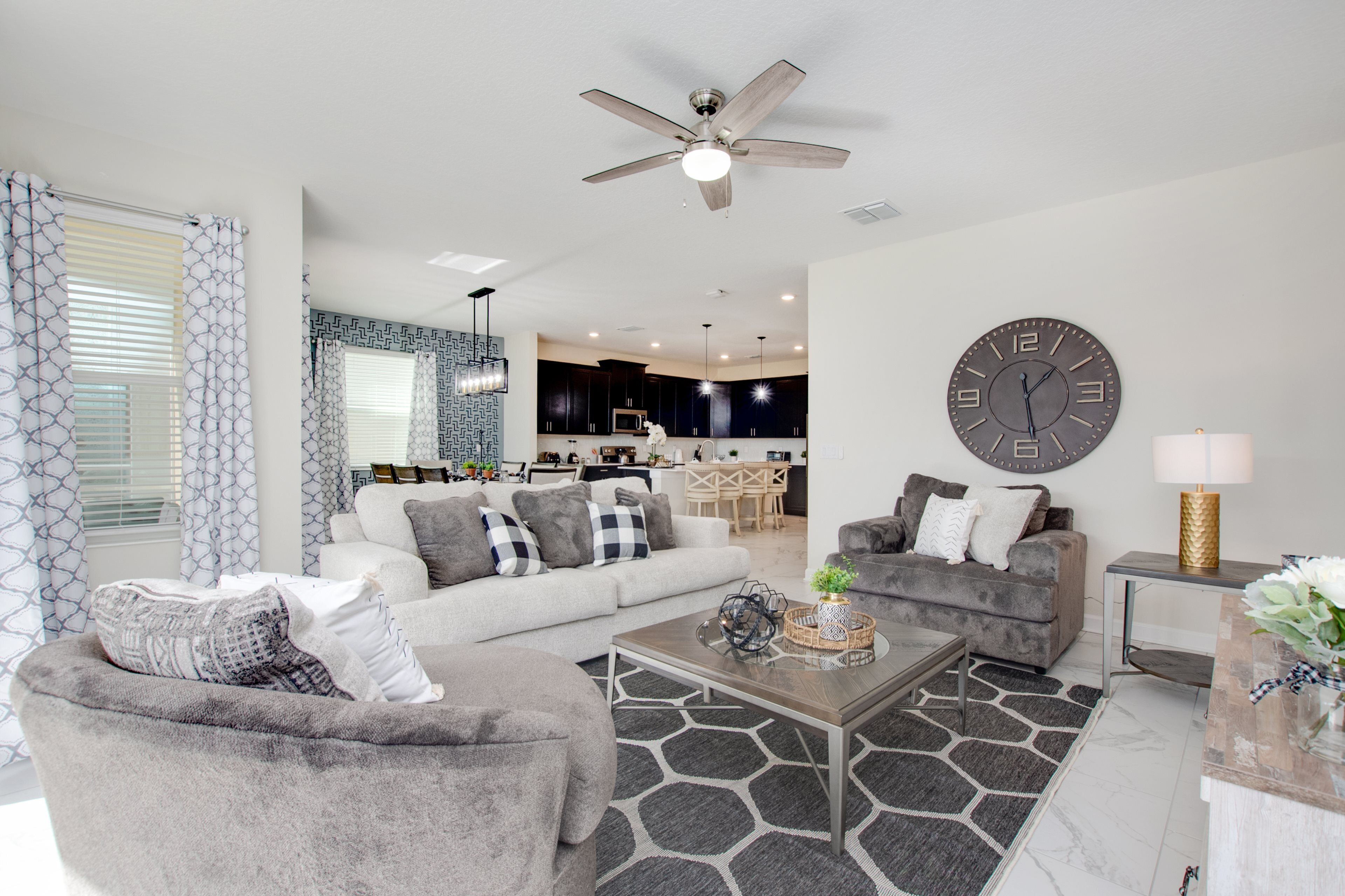 A modern living room with a sofa, armchair, coffee table, and a large wall clock.