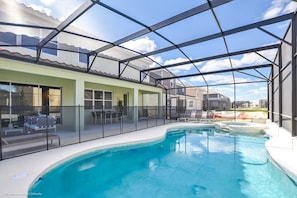 A pool area with a glass enclosure, lounge chairs, and a view of neighboring houses.