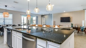 Una cocina moderna con una isla central, iluminación colgante y un área de comedor con sofá y sillas.