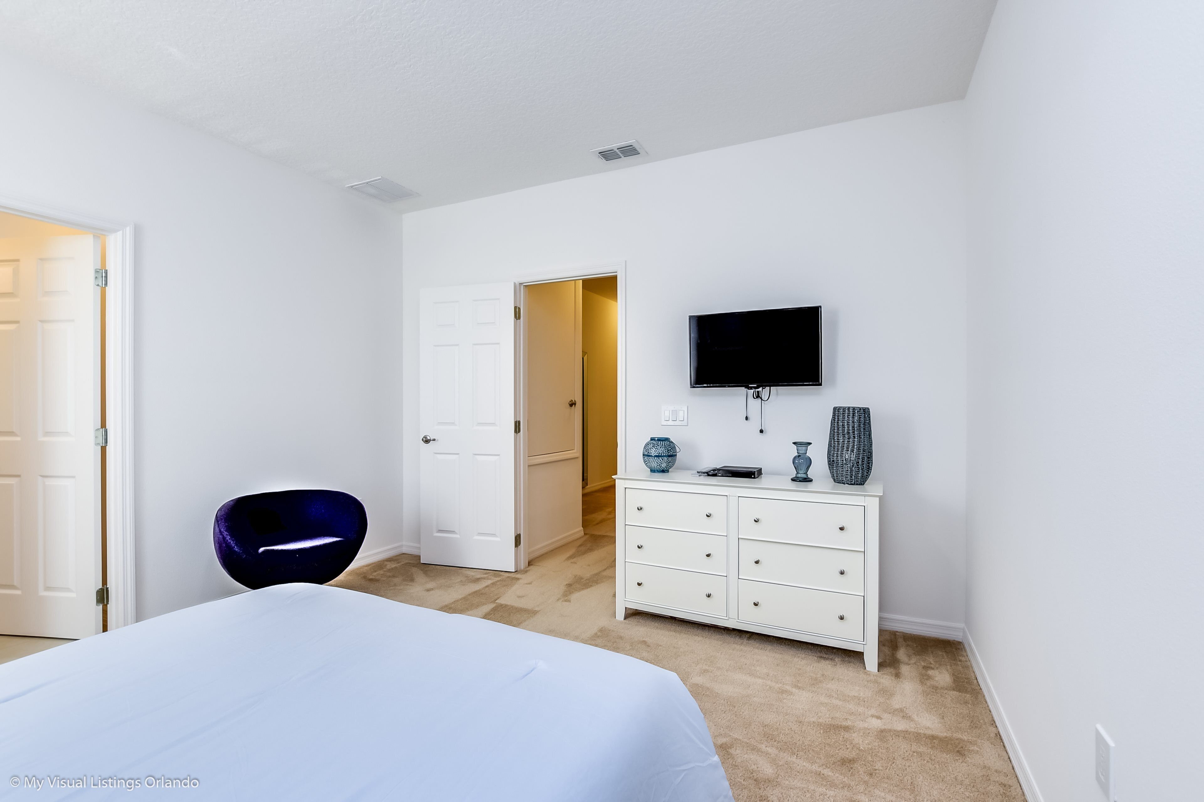 A bedroom with a bed, a dresser, a television, and a chair.
