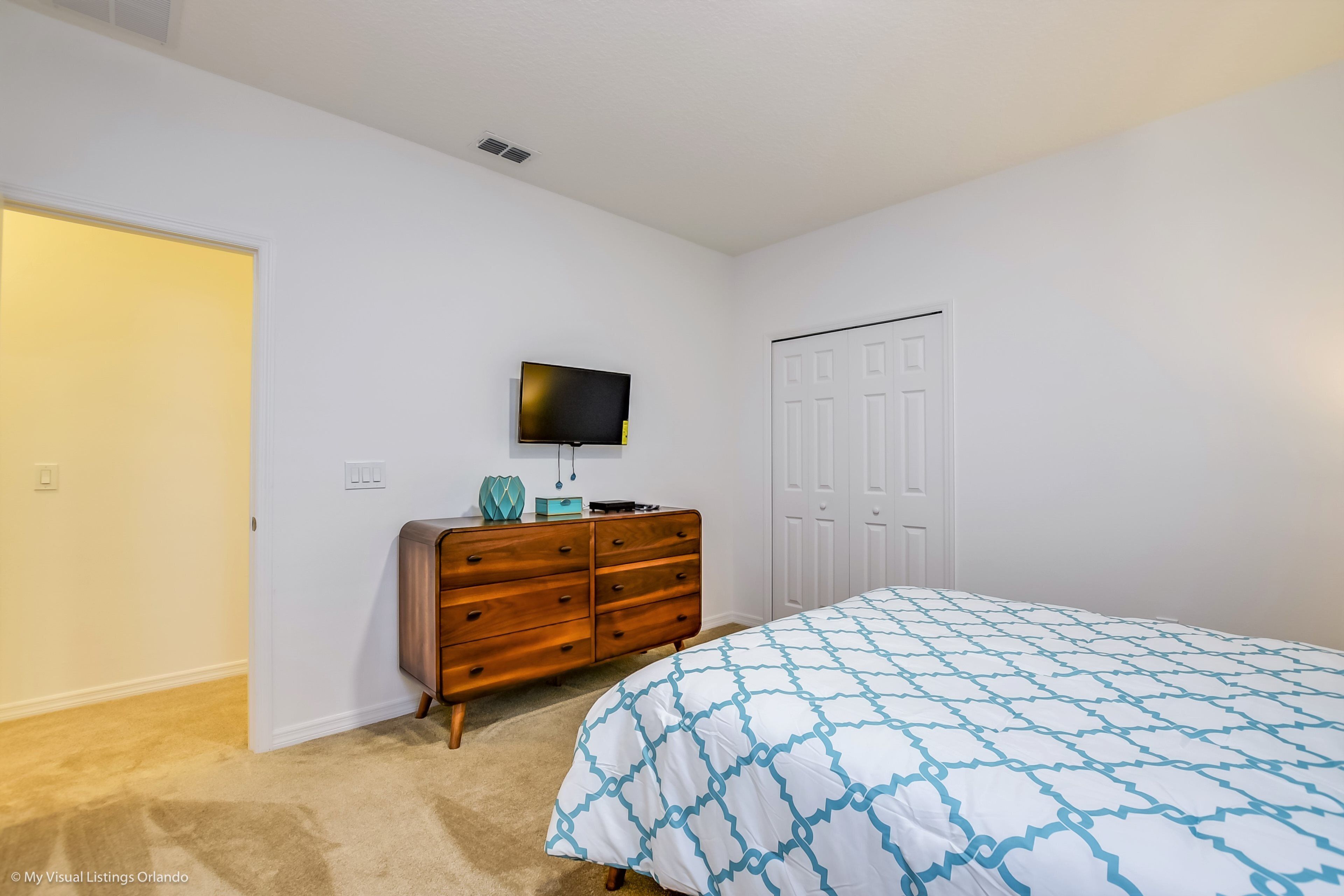 A bedroom with a bed, dresser, television, and closet.