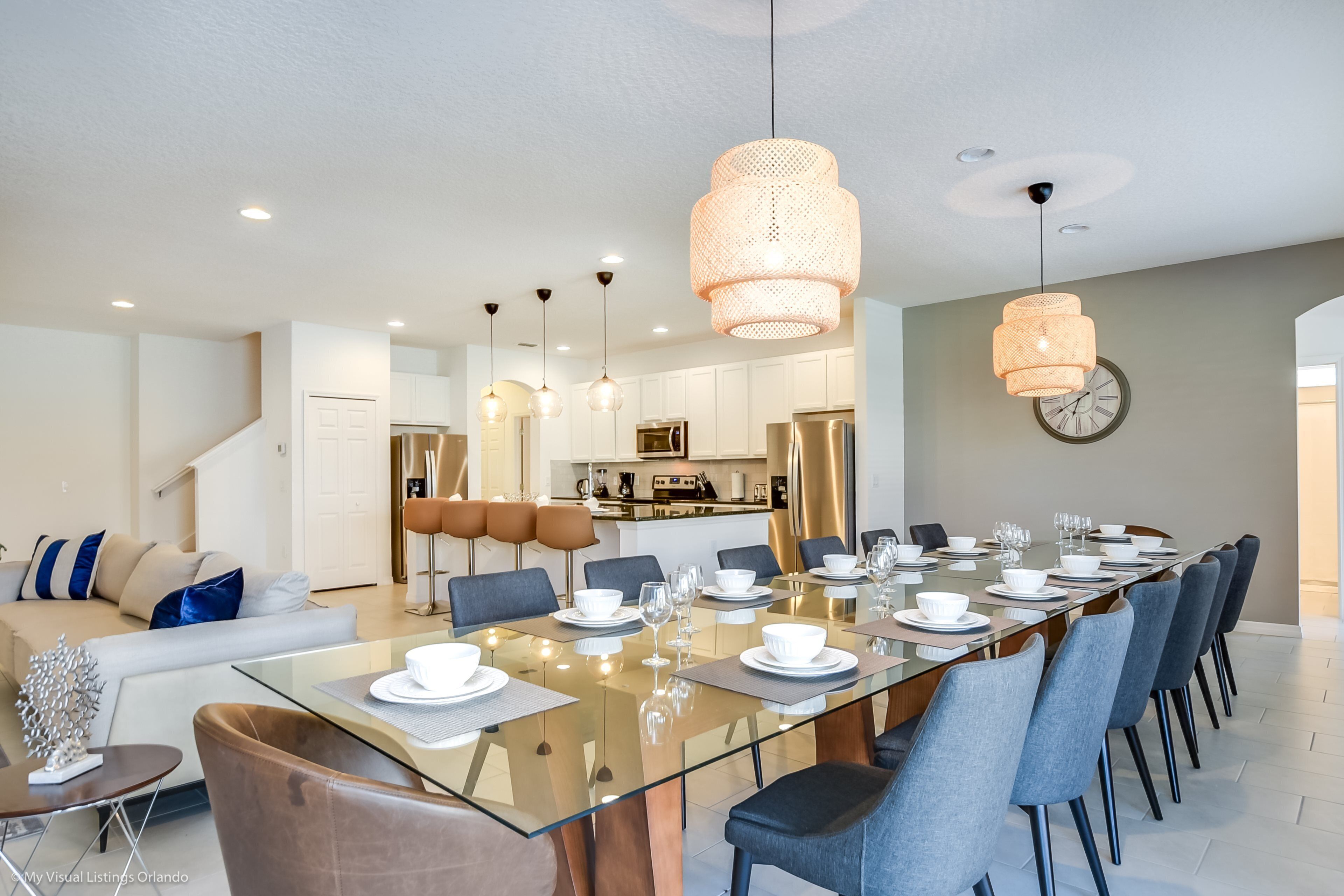 A modern dining area with a glass-top table, blue chairs, and pendant lighting.