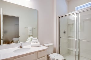 A bathroom with a white sink, mirror, toilet, and glass shower enclosure.