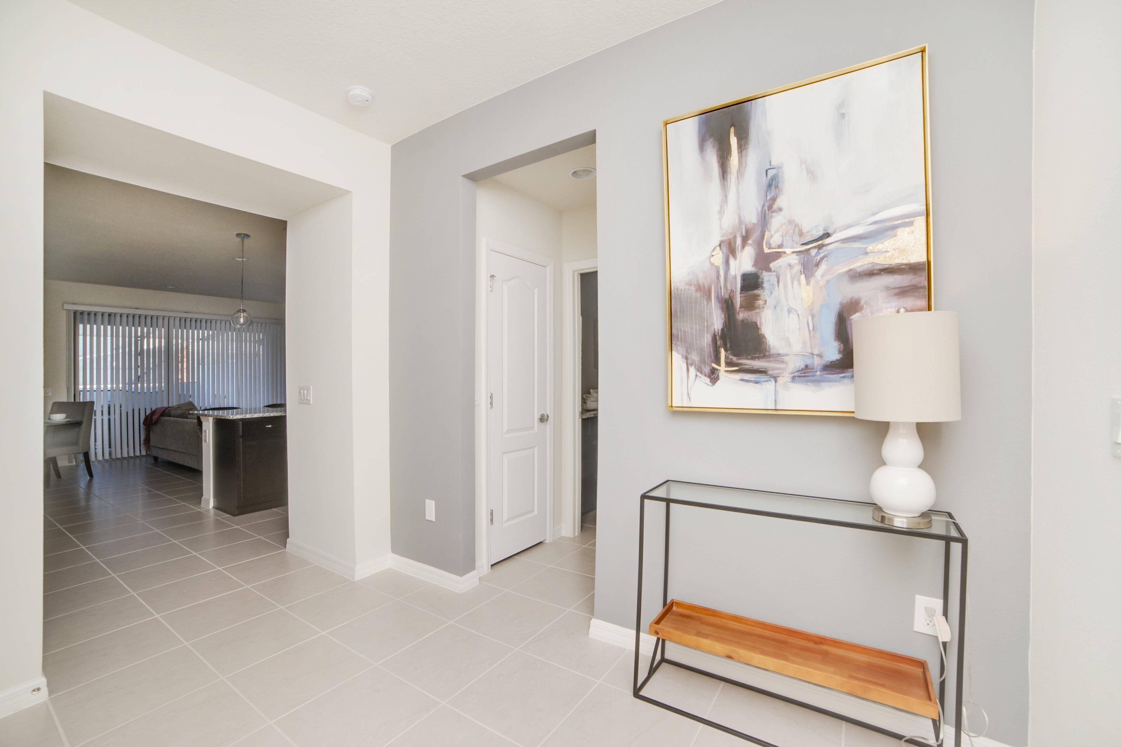 A modern interior with a hallway leading to a dining area, a minimalist console table, and a large abstract painting.