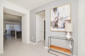 A modern interior with a hallway leading to a dining area, a minimalist console table, and a large abstract painting.