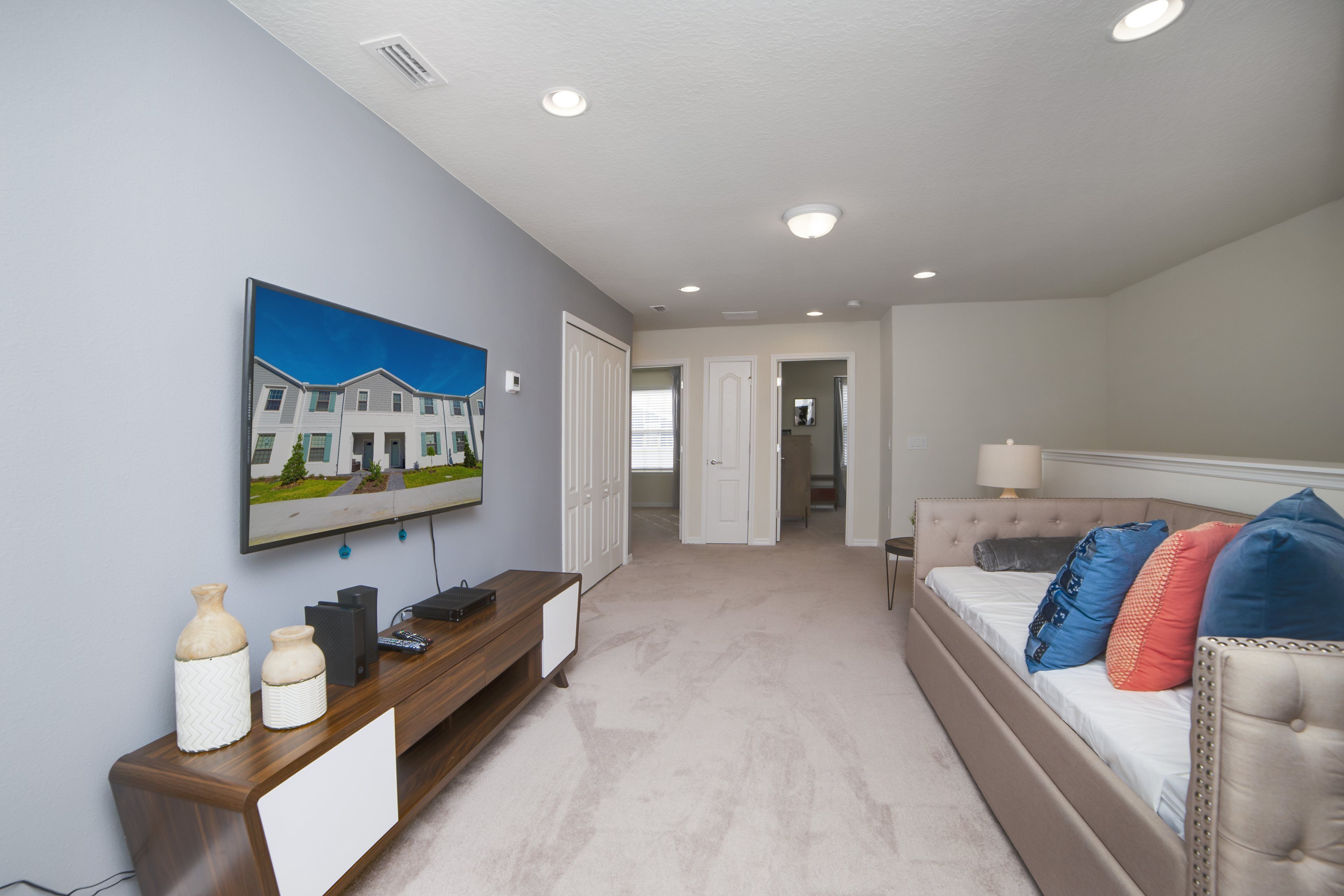 Un dormitorio con una cama, un televisor montado en la pared, un aparador y una puerta que da a otra habitación.