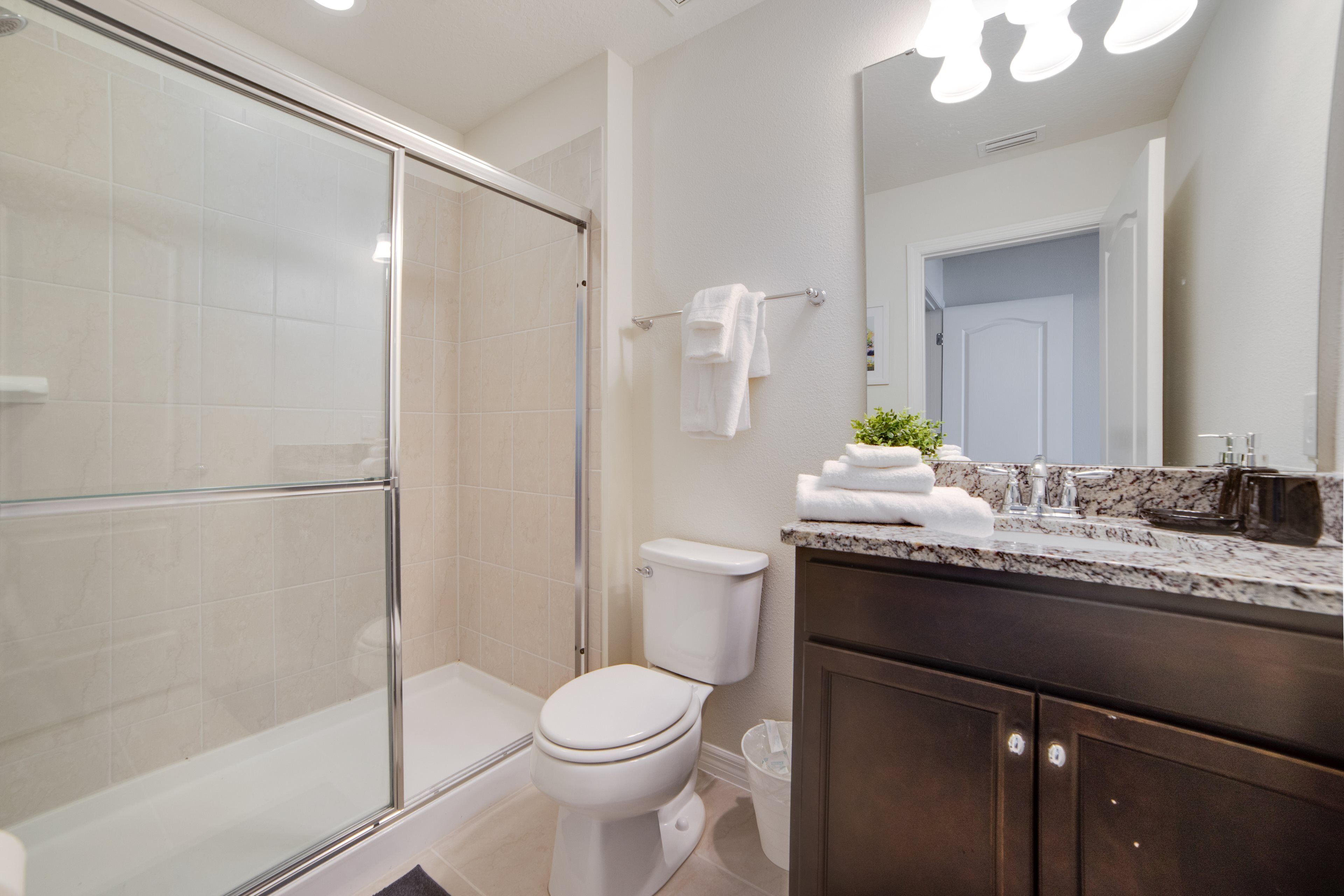 A modern bathroom with a glass shower enclosure, a toilet, a sink with a marble countertop, and a mirror above the sink.