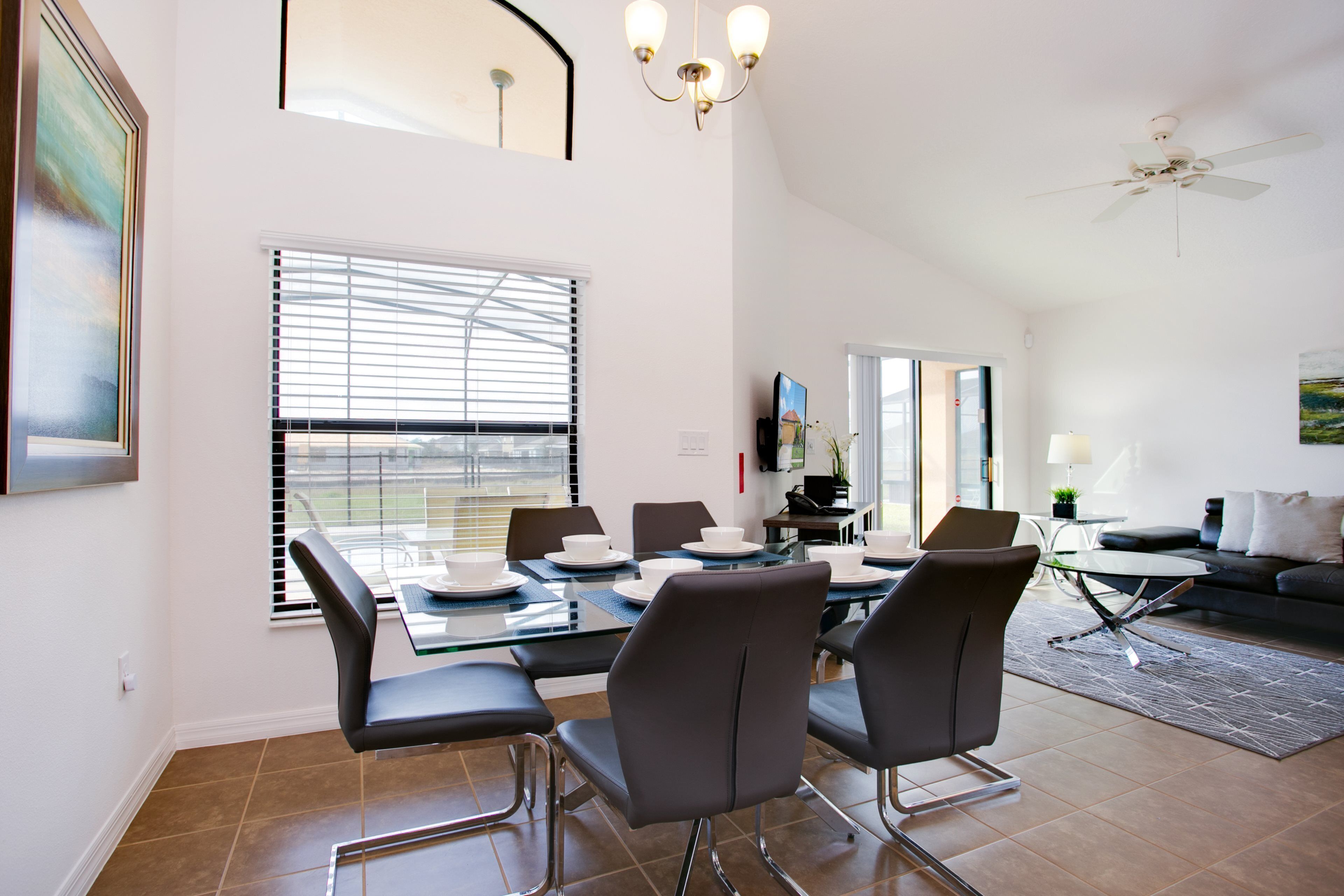 A dining area with a glass table, black chairs, and a ceiling fan.