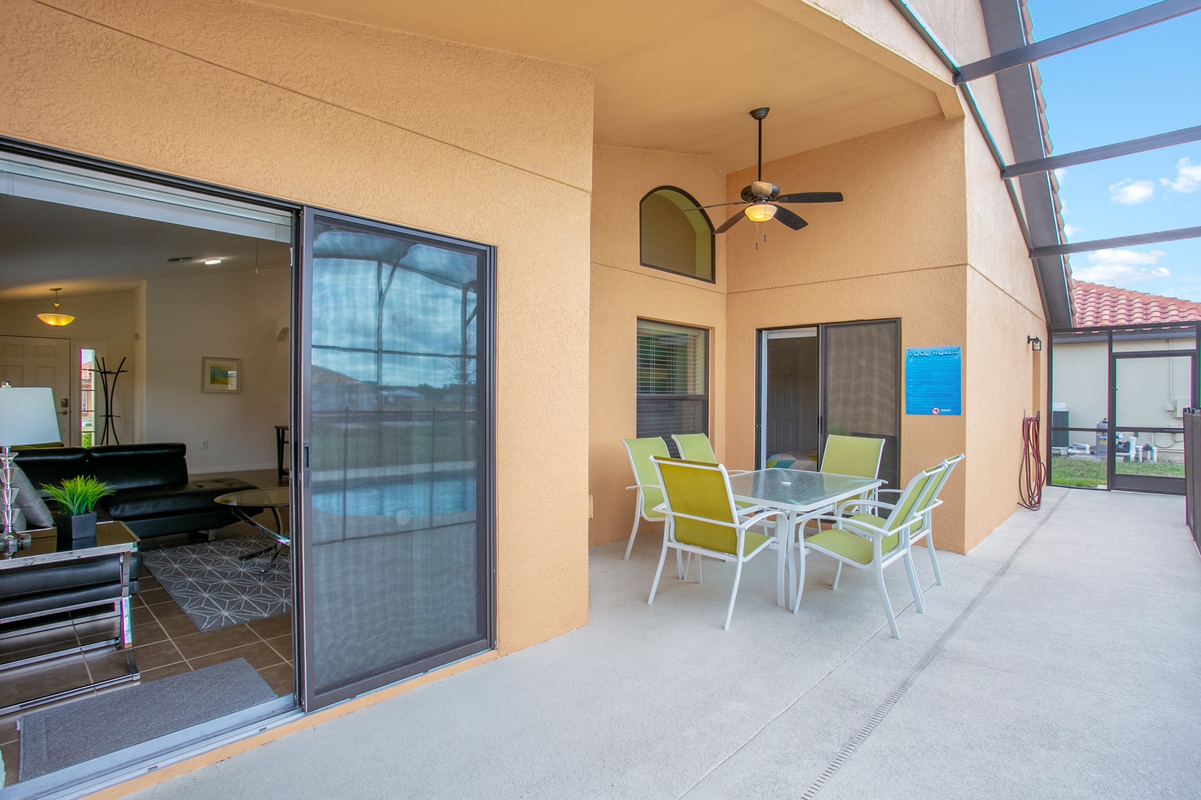 A covered patio area with a table and chairs, a ceiling fan, and a sliding glass door leading to an interior space.