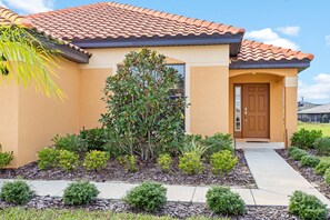 A two-story house with a tiled roof, a front door, and a small garden with various plants and shrubs. - 2569rosemont (Davenport)