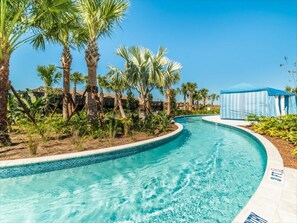 Ein Pool mit geschwungener Kante, umgeben von Palmen und blauem Himmel.