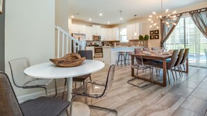 A modern kitchen with a dining area, featuring a round table with chairs, a staircase, and a large window with curtains. - 6 Bedroom 5 Bathroom Vacation Home (Davenport)