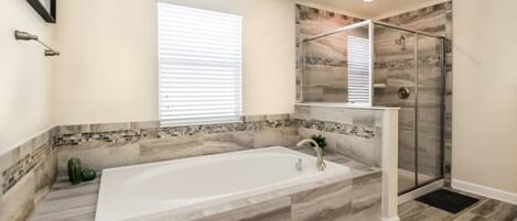 A bathroom with a large bathtub, a shower enclosure, and a tiled backsplash.