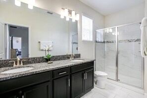 A modern bathroom with two sinks, a large mirror, and a glass shower enclosure.