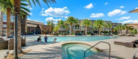 A pool area with lounge chairs and palm trees, surrounded by buildings with a modern architectural style.