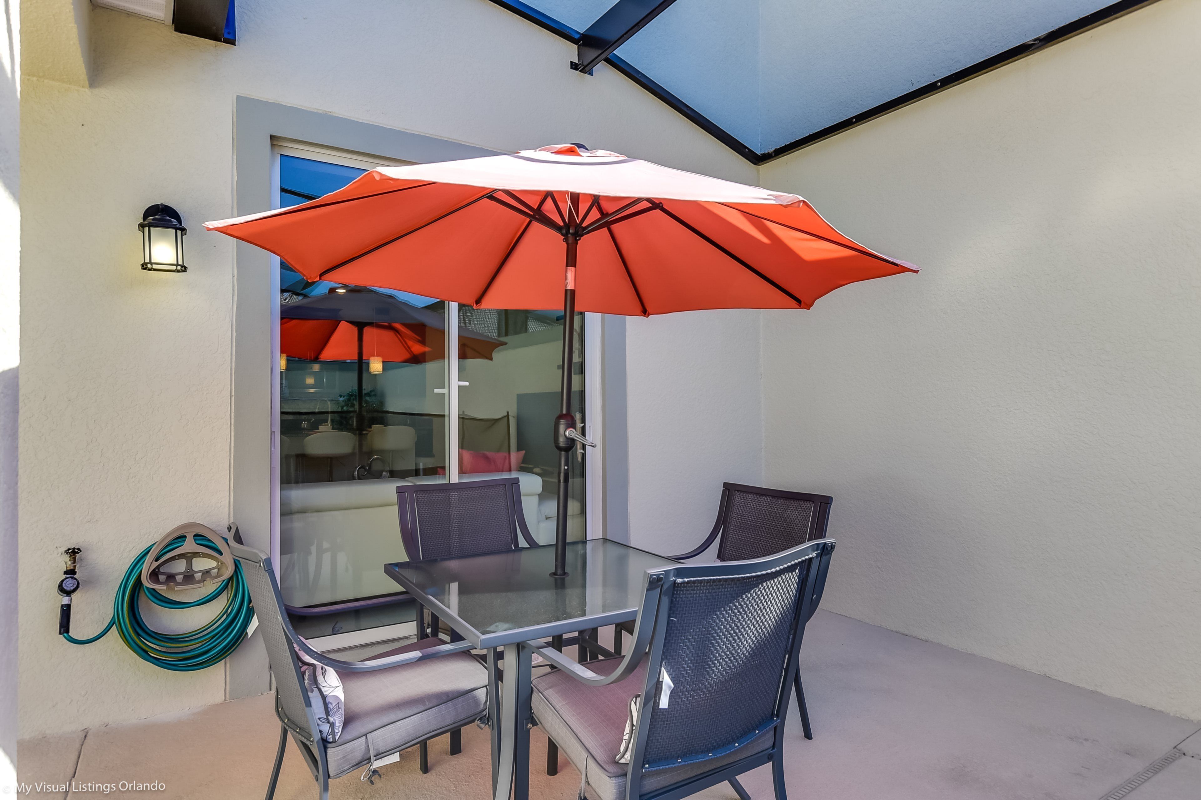 A glass-top table with four chairs and a large orange umbrella.