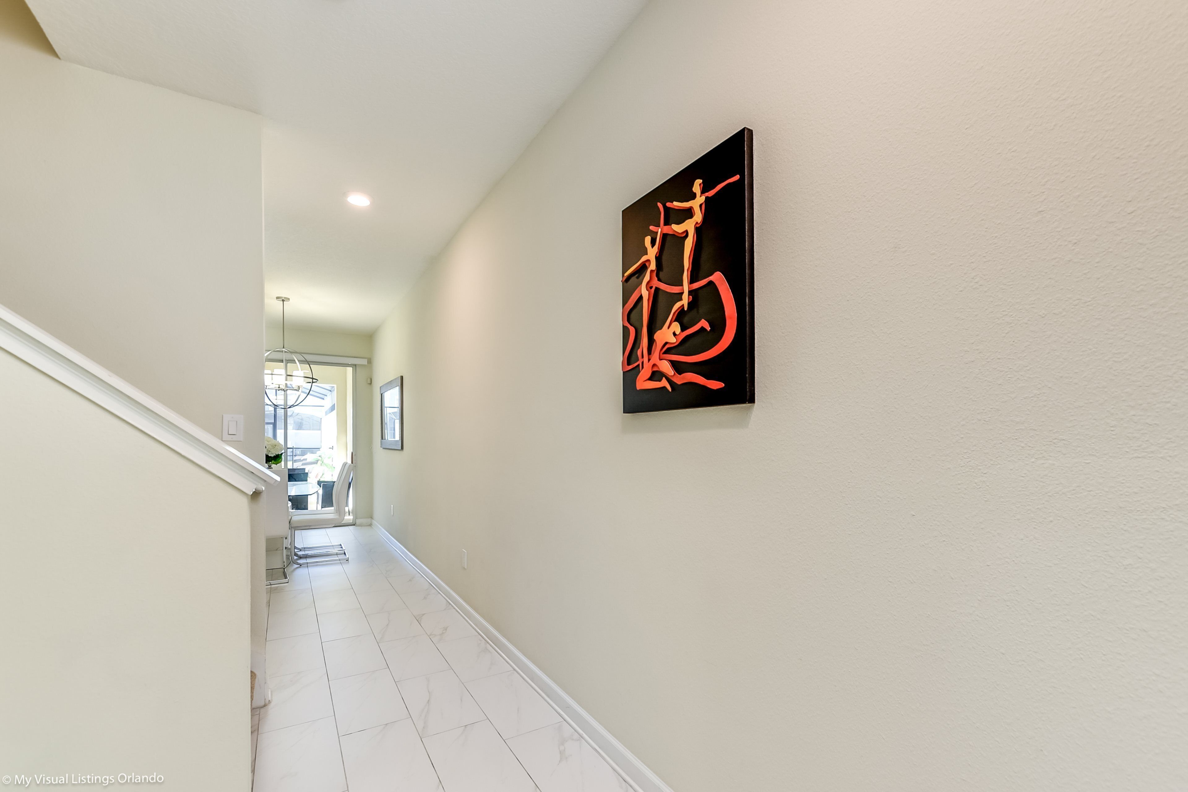 A hallway with a staircase, a modern art piece on the wall, and a view into another room.