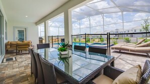 A spacious patio with a glass table and wicker chairs, overlooking a swimming pool and a residential area.