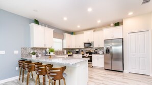 A modern kitchen with white cabinets, a granite countertop, stainless steel appliances, and a central island with bar stools.