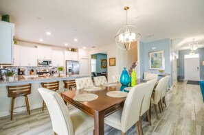 A spacious dining area with a wooden table and white chairs, a kitchen with white cabinets and a microwave, and a blue accent wall. - 6 Bedroom Champions Gate Villa (Davenport)