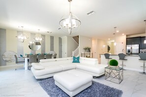 A modern living room with a white sectional sofa, a glass coffee table, and a staircase leading to the upper floor.