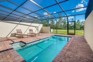 A swimming pool with a glass enclosure, lounge chairs, and a view of the outdoors. - 4bed 3Ba Home With Pool at Windsor (Kissimmee)