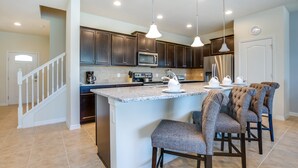A modern kitchen with dark wood cabinets, a granite countertop, and a central island with bar stools. - 4bed 3Ba Home With Pool at Windsor (Kissimmee)