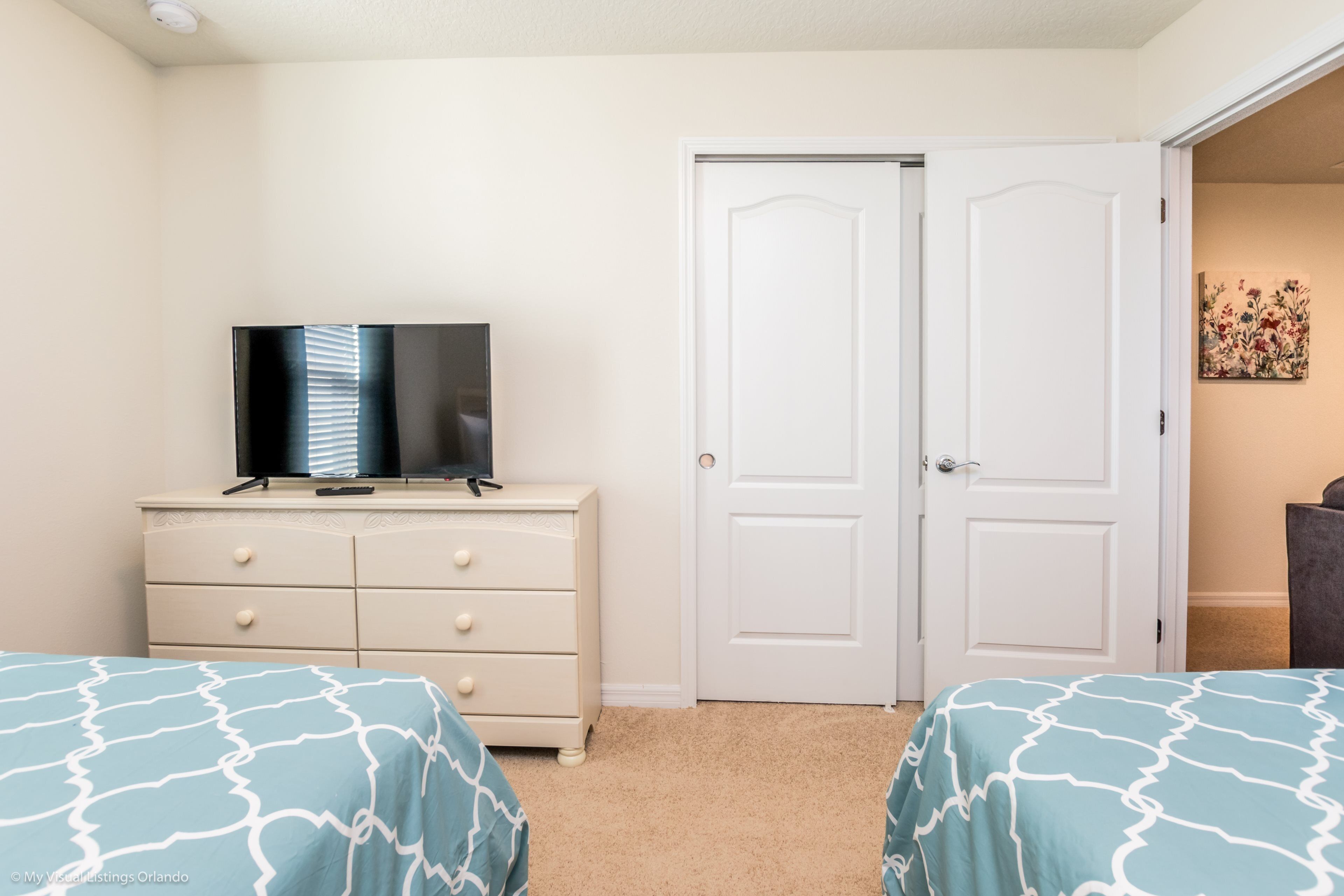 Une chambre avec deux lits, une commode, un téléviseur et une porte blanche.