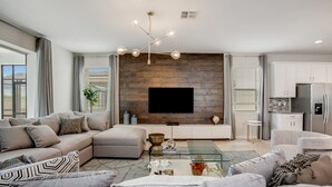 A modern living room with a sectional sofa, a glass coffee table, and a flat-screen TV mounted on a wooden wall. - 9 BD 6.5 BH With Pool, Spa and GR (Kissimmee)