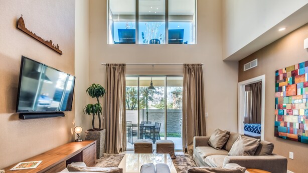 A modern living room with a flat-screen TV, comfortable seating, a coffee table, and a view of the outdoors. - Magic Village Resort 4 Bdrm Townhome (Kissimmee)