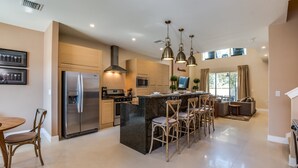 A modern kitchen with a central island, stainless steel appliances, pendant lighting, and a dining area with wooden chairs. - Magic Village Resort 4 Bdrm Townhome (Kissimmee)