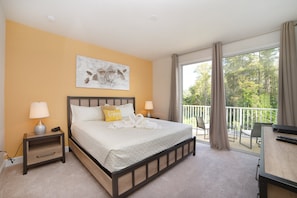 A bedroom with a bed, bedside tables, a desk, and a balcony with a view of trees.