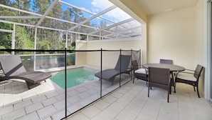 Et overdækket udendørs område med swimmingpool, liggestole og et bord.