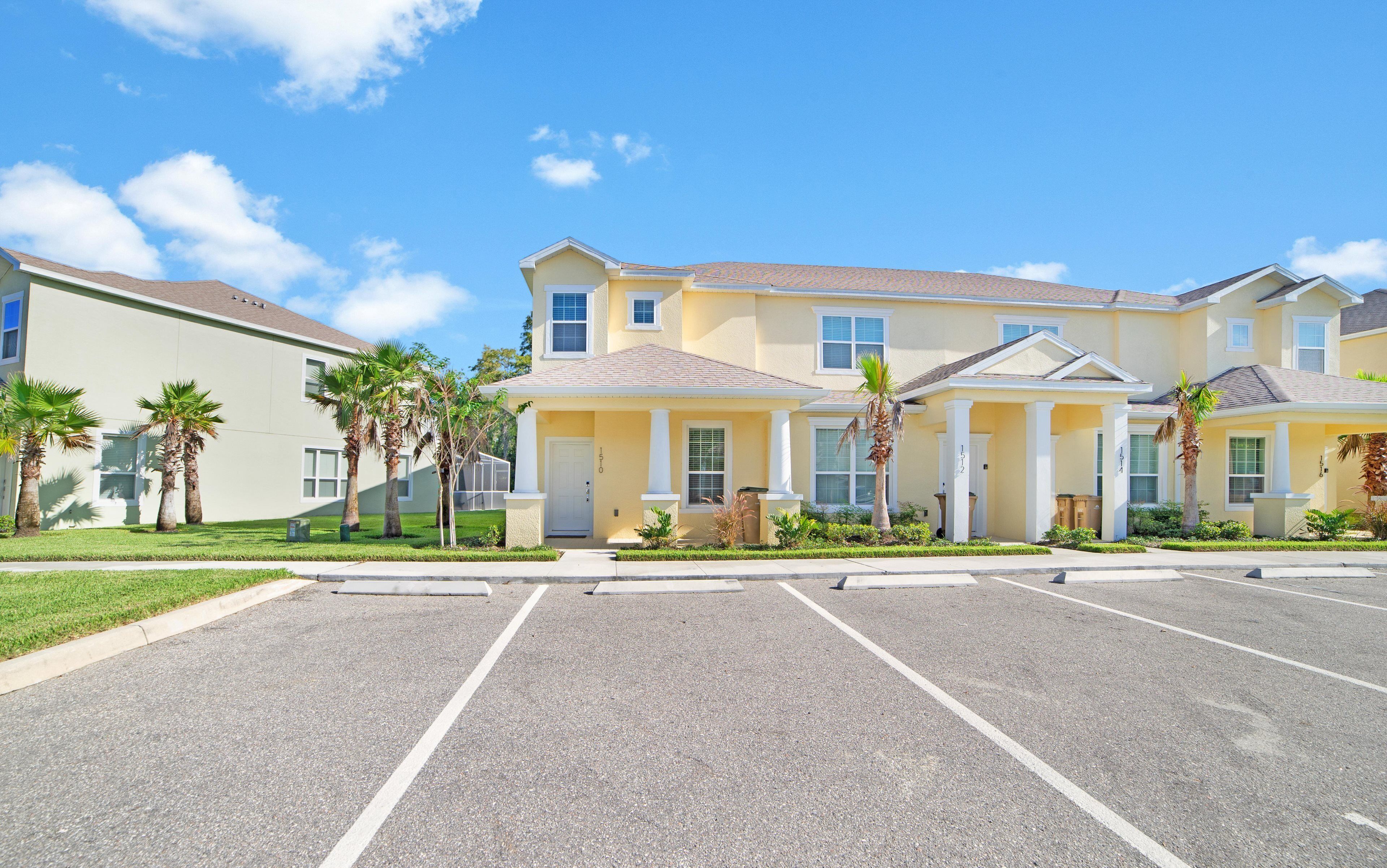A row of yellow townhouses with a parking lot in front.