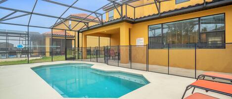 A pool area with a glass enclosure, outdoor seating, and a yellow building with windows.