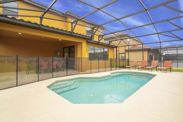 An indoor swimming pool with a glass ceiling, surrounded by lounge chairs and a covered patio area.