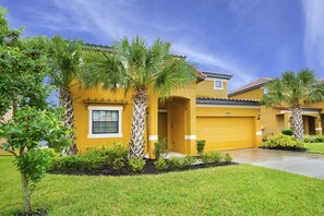 A yellow house with a garage, surrounded by well-maintained lawns and palm trees.