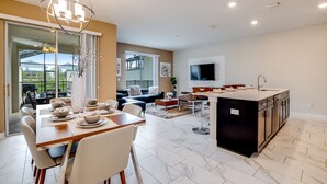 A spacious living area with a dining table set for four, a kitchen with a large island, and a sliding glass door leading to an outdoor patio. - 4 Bed 3 Ba Champions Gate Pool Home (Davenport)