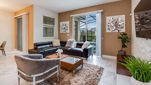 A modern living room with a black leather sofa, a wooden coffee table, and a fluffy rug. There is a large window with a view of greenery outside. - 4 Bed 3 Ba Champions Gate Pool Home (Davenport)