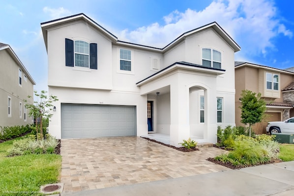 A modern two-story house with a garage, a well-maintained lawn, and a brick driveway. - 9 Bdrm 6,5 B Villa W Private Pool (Kissimmee)