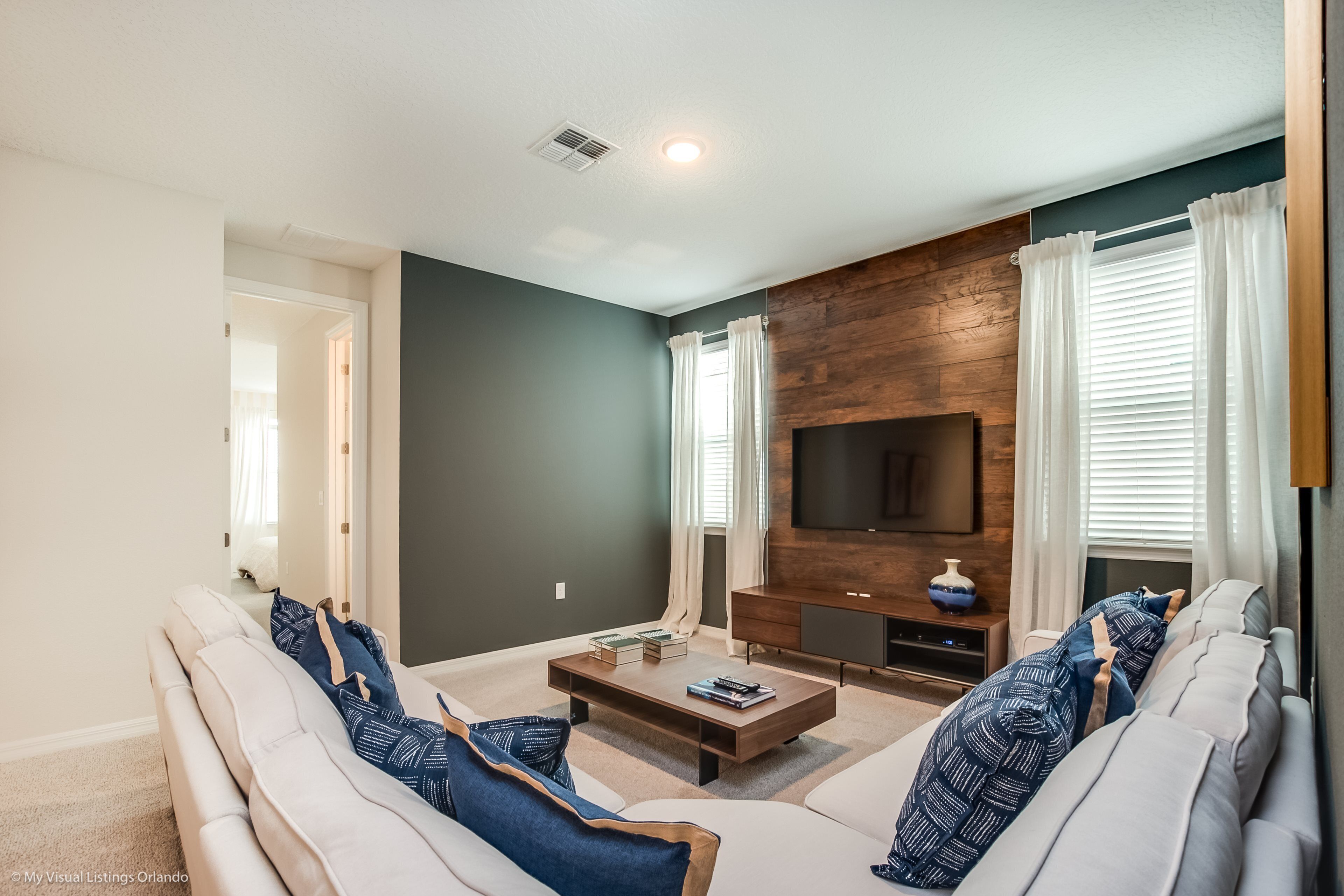 A modern living room with a sectional sofa, a coffee table, a flat-screen TV, and a wooden accent wall.
