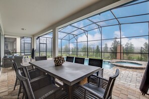 A spacious patio with a dining area, a hot tub, and a view of a swimming pool and greenery. - 9 Bdrm 6,5 B Villa W Private Pool (Kissimmee)