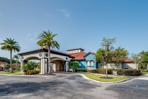 A gated community entrance with a covered driveway, palm trees, and houses with red-tiled roofs. - 518mb New and Modern 8 Bedroom 5 Bathroom Villa (Kissimmee)