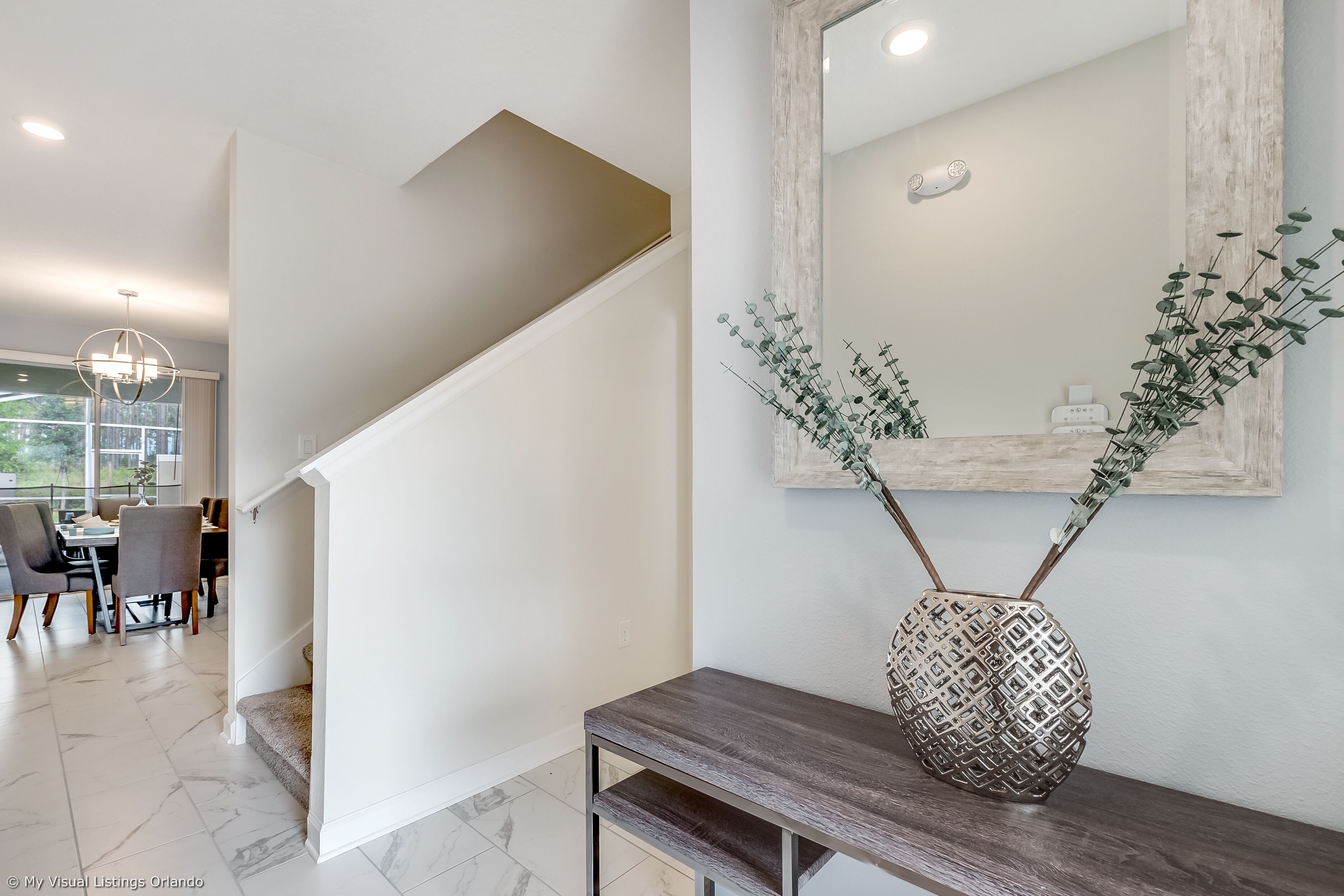 A modern interior with a staircase, dining area, and a decorative vase on a console table.
