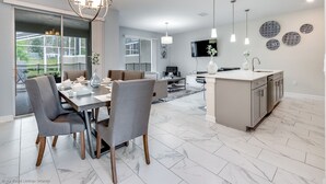 A modern kitchen with a central island, pendant lighting, and a dining area with grey upholstered chairs. - Relaxing 4bed 3Ba Champions Gate Pool (Davenport)