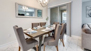 A dining area with a rectangular table, six chairs, a chandelier, a large mirror, and a sliding glass door leading to a balcony. - Relaxing 4bed 3Ba Champions Gate Pool (Davenport)