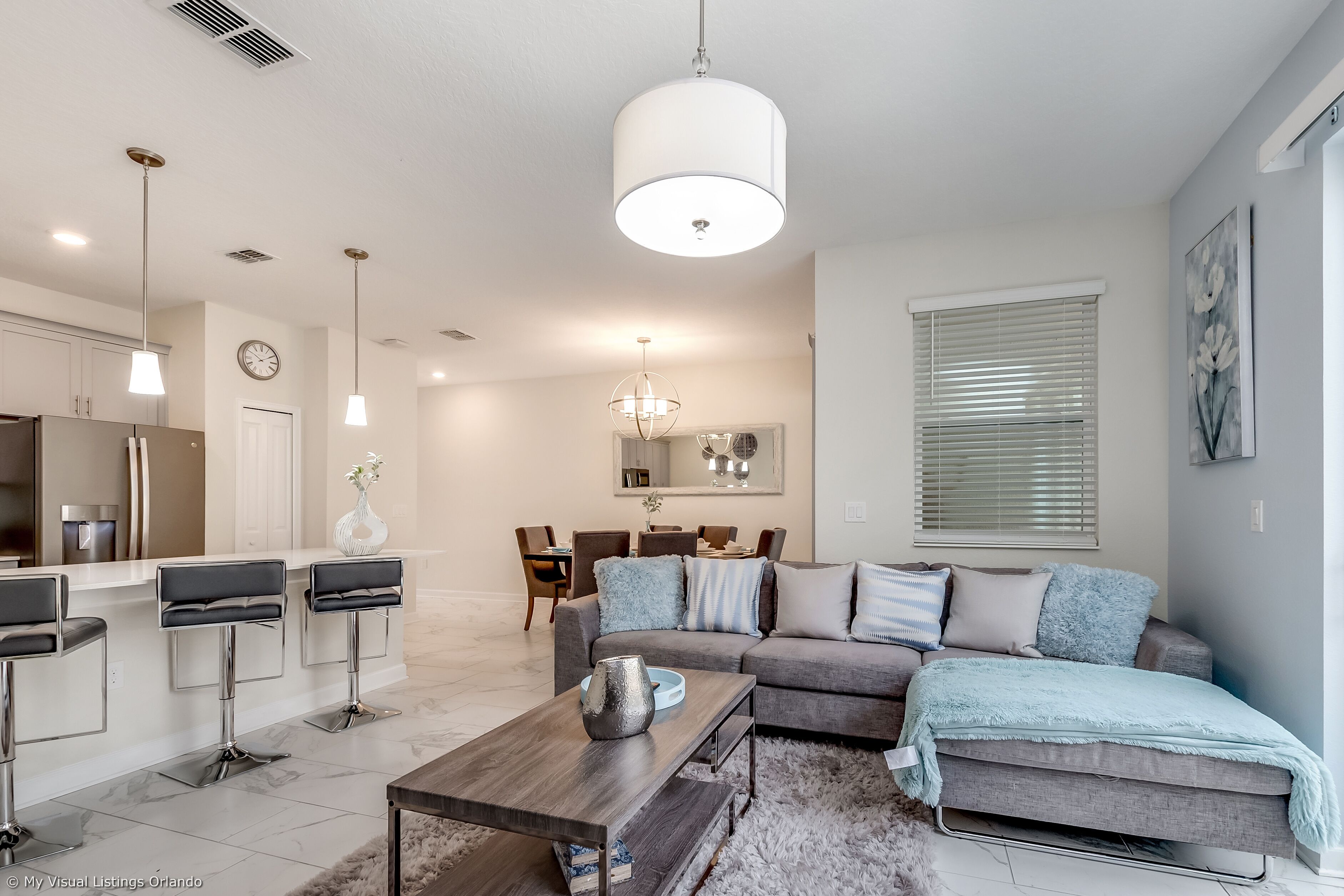 A modern living room with a gray sofa, a coffee table, and a dining area in the background.