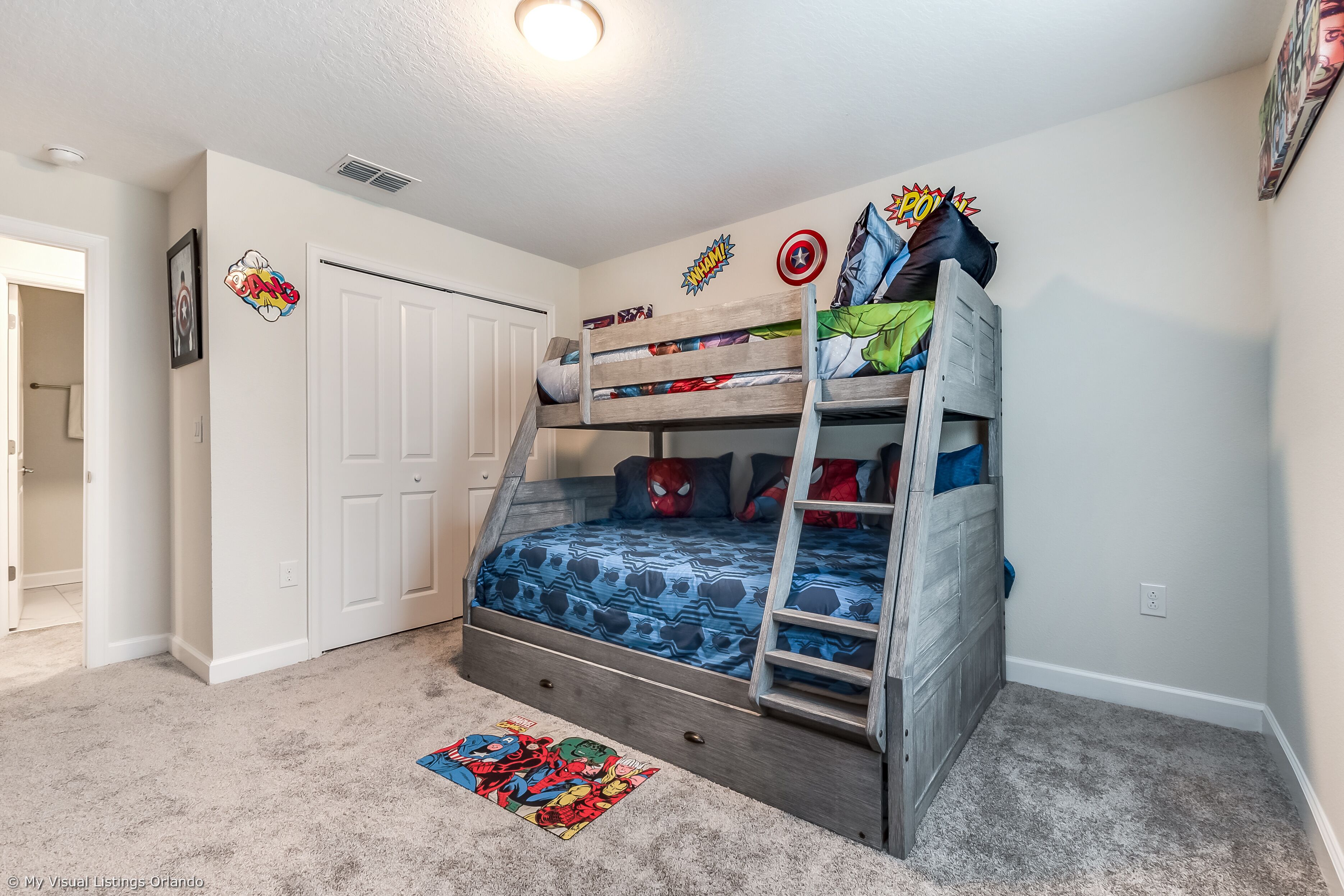 A bunk bed with a ladder, a closet, and superhero-themed wall decals.